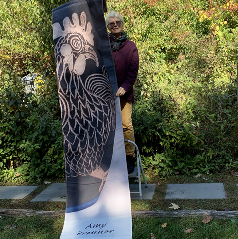 Amy Brenner holding up her banner showing pottery vase Rooster design