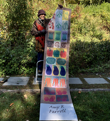 Amy R Farrell holding up her banner with depictions of multi color blocks of vegetables