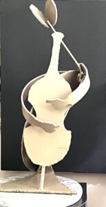 beige painted cut and designed, seated metal sculpture figure playing the cello