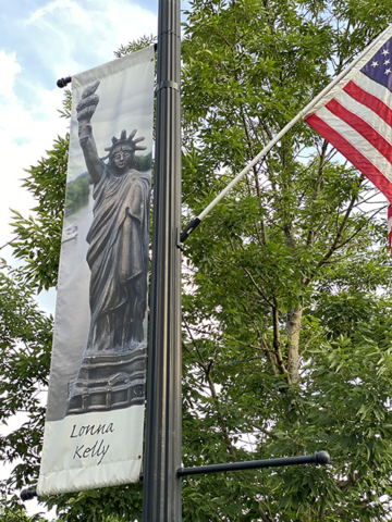 Lonna Kelly banner of Statue of Liberty against green leafy tree