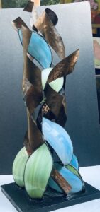 recylcled stained glass pieces with twisted copper ribbons attached to and pointing upward from a black wooden base