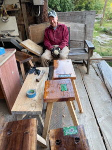 Julian M Strauss with benches - a scene with artist at rest among collection of wood benches in process. Each bench (wifi platform) has a computer mother board embedded in the wood, with a seal of resin.