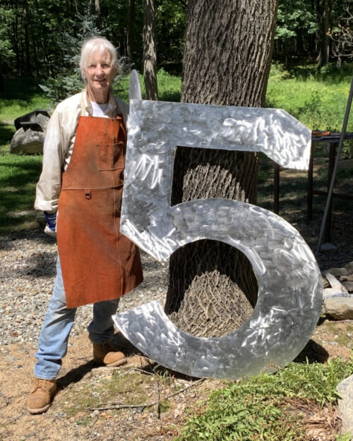 Metal sculpture standing by a large number five she's created