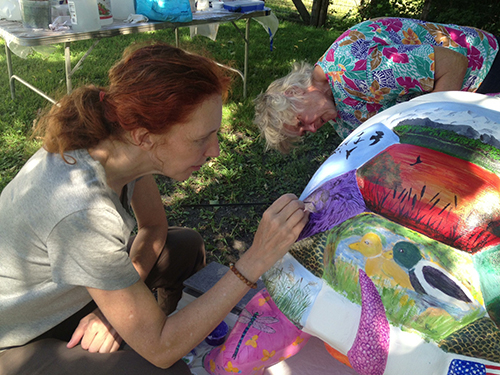 two artists at work on turtle in grassy yard