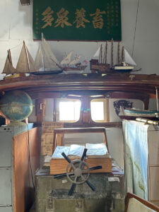 art installation at window with boat models and boat parts, maps, globe, telescope, nautical books