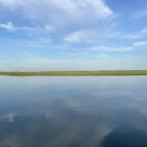 blue sky with white clouds reflect in still bay water bisected gy a strip of green land