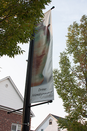 Drew Montgomery pottery jar on banner with trees and buildings in background