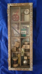 mixed media – glass fronted shadow box with vintage items; compass, baseball card, sewing notions, blocks and more.